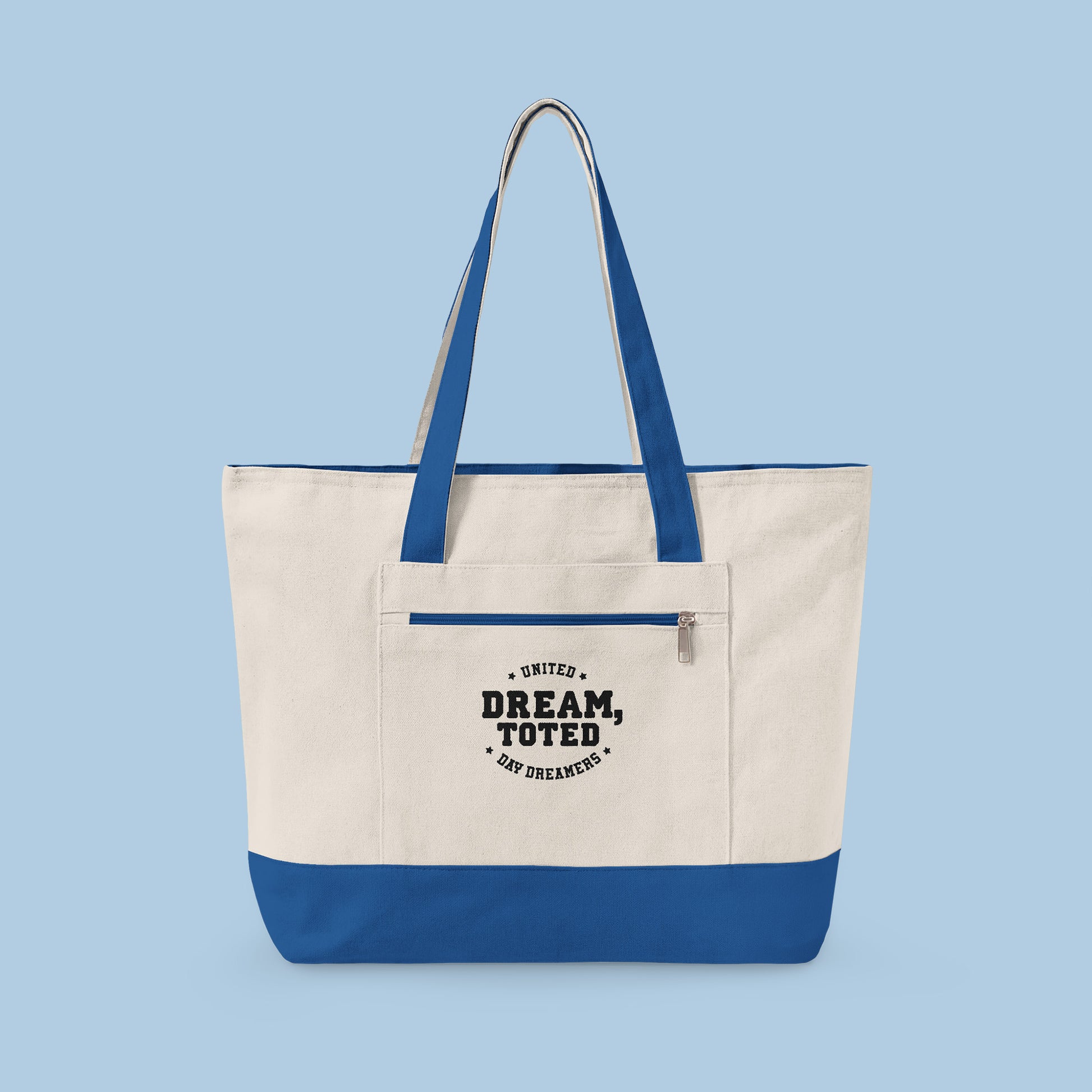 Beige tote bag with blue accents and text that reads, Dream, Toted. United Day Dreamers on a light blue background
