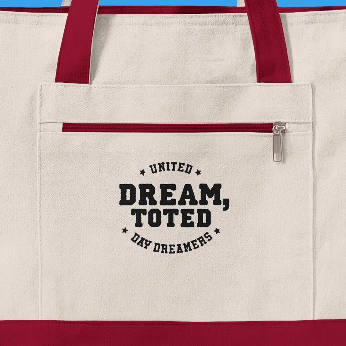 Beige tote bag with red handles and text on a blue background