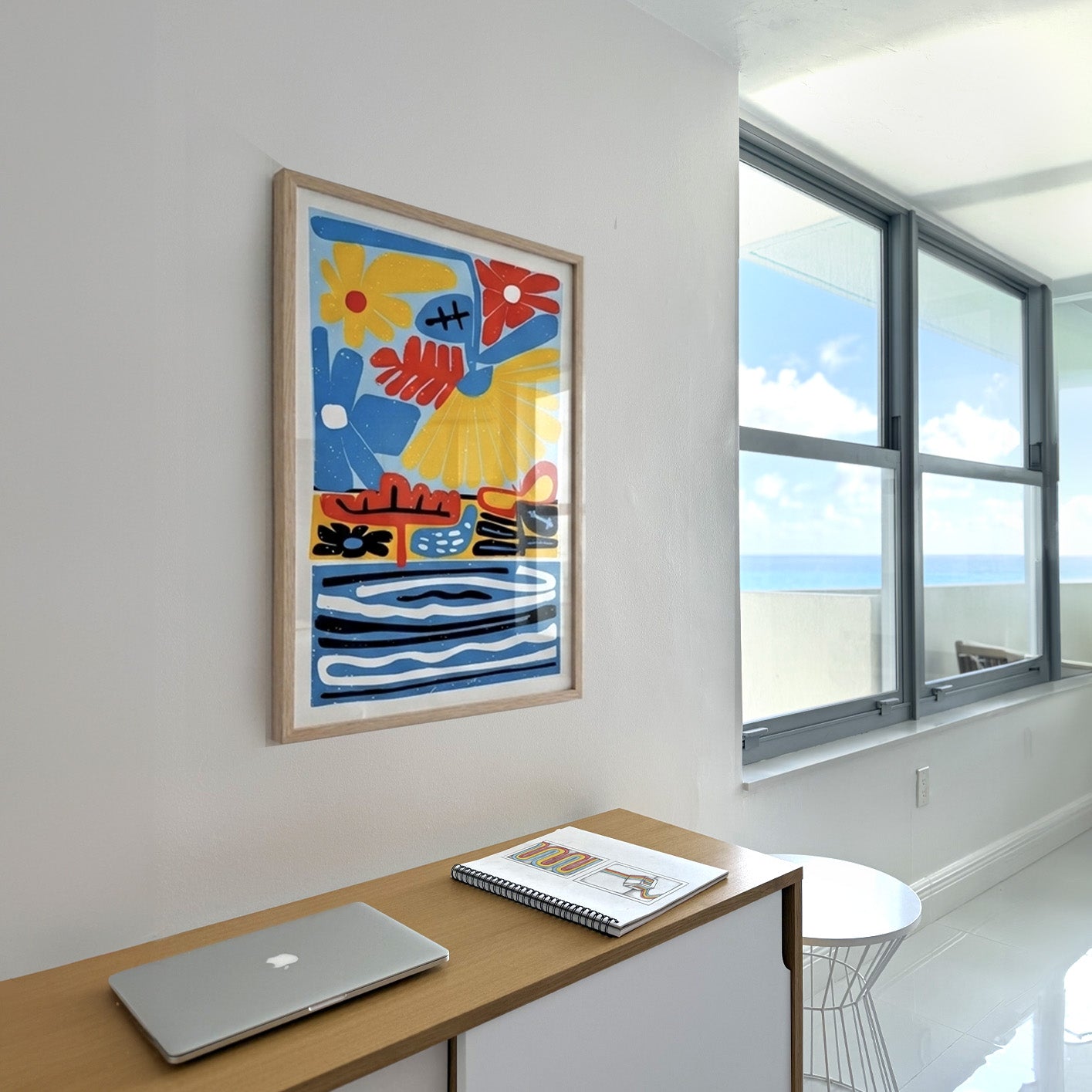 Colorful abstract artwork on a wall above a desk with a laptop in an apartment wall by the sea.