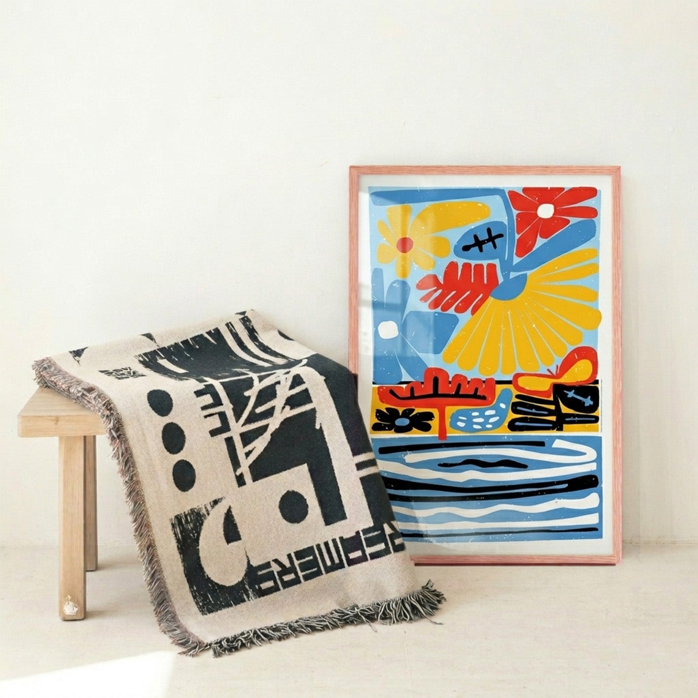 Framed abstract artwork with colorful design next to a patterned throw blanket on a light surface.