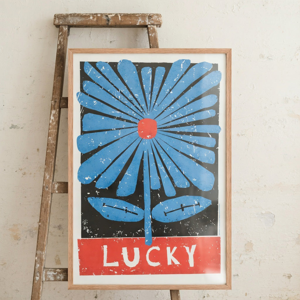 Framed artwork with blue floral design and red text on a wooden easel against a textured wall.