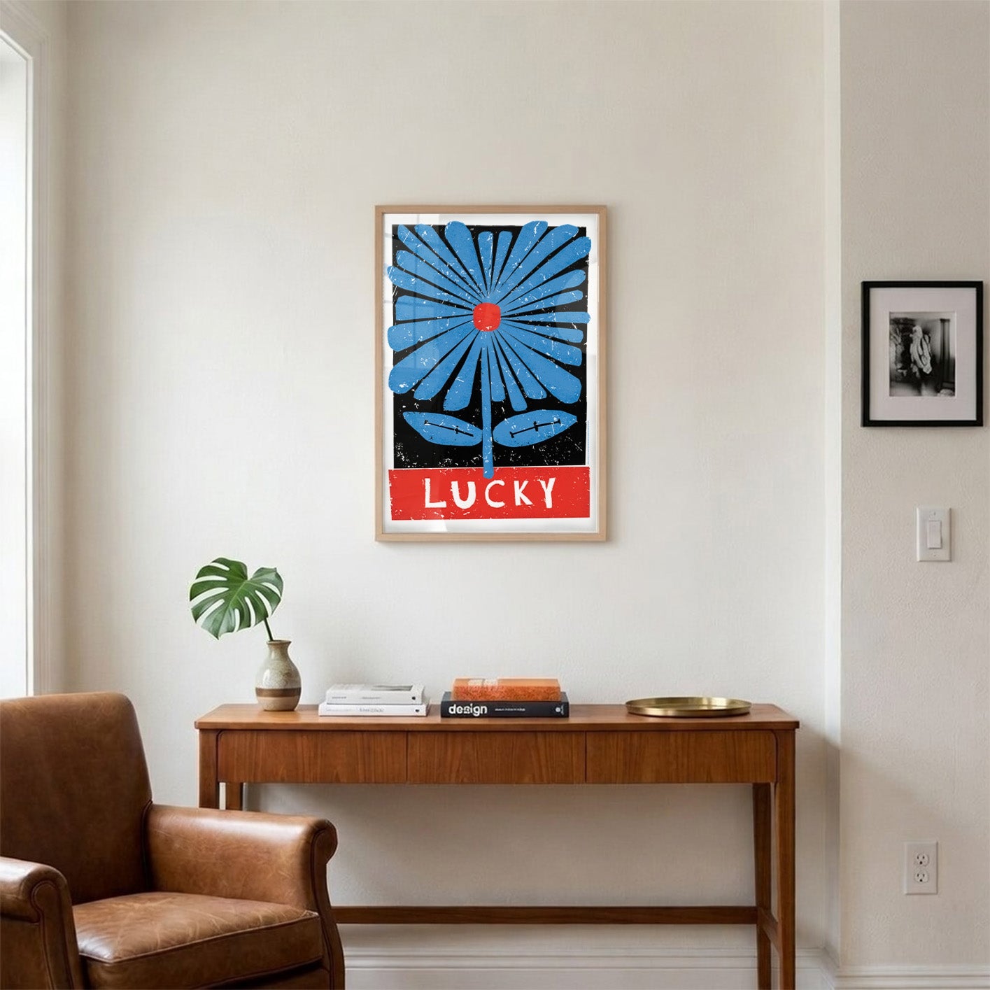 Framed artwork with a blue flower and 'LUCKY' text on a wall above a wooden console table.