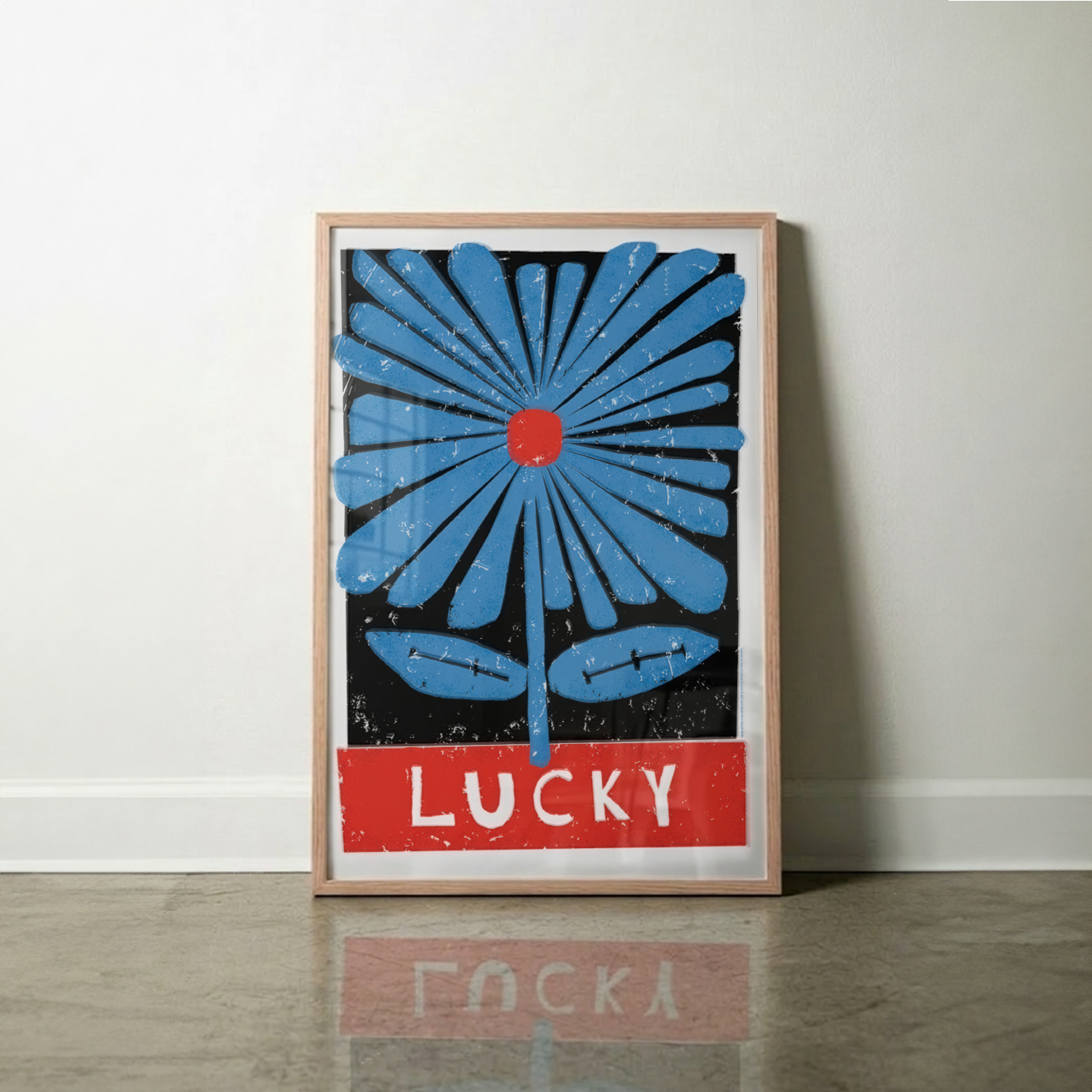 Framed artwork with a large blue flower and white 'LUCKY' text on a red block on white wall.