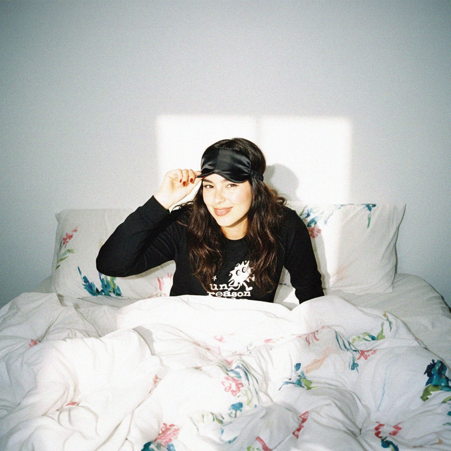 Woman sitting on a bed with floral bedding and a plain background