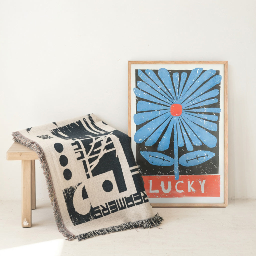 Decorative throw blanket with geometric pattern and framed artwork with blue flower design on a white background