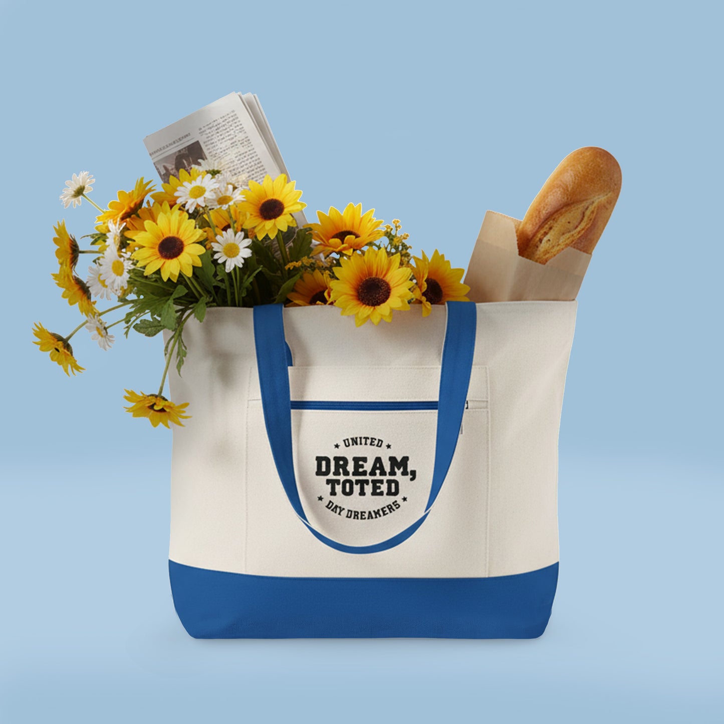 Tote bag with flowers and bread on a blue background. The tote is Beige with blue accents and text that reads, Dream, Toted. United Day Dreamers on a light blue background