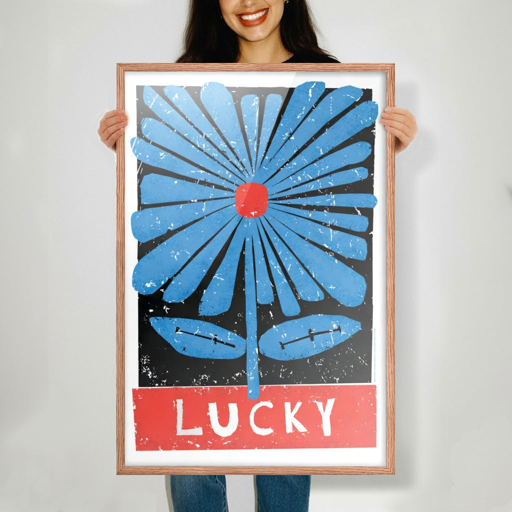 Person holding a framed poster with a blue flower and red text on a gray background, Frame color is natural wood. 
