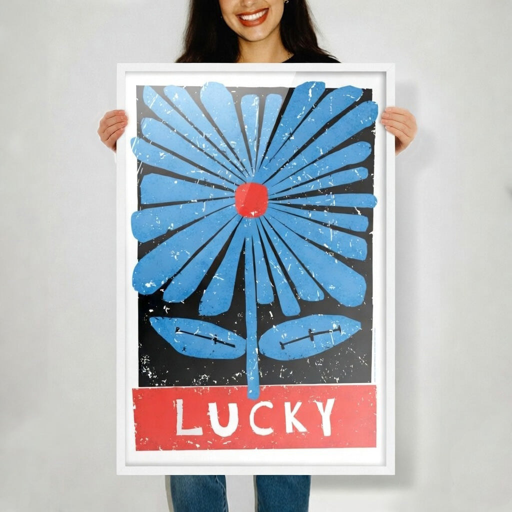 Person holding a framed poster with a blue flower and red text on a gray background, Frame color is white. 